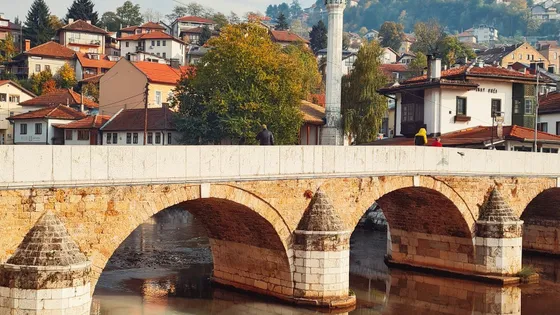 Bridge over the Miljacka River at sunrise with mosque minarets and Sarajevo old town buildings reflected in the calm water, Bosnia
