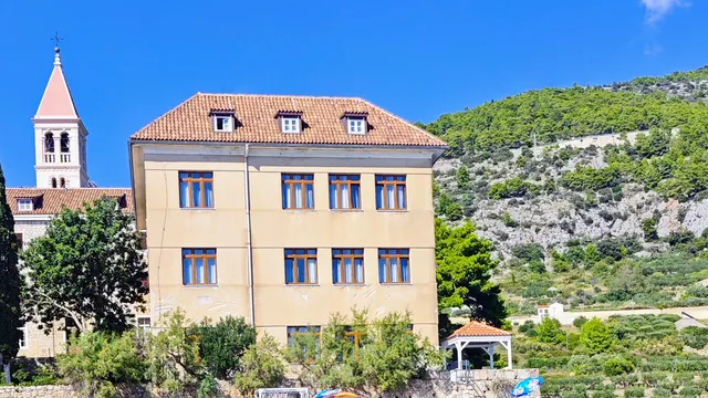 Historic Franciscan Monastery and bell tower on Hvar island's rocky coast, viewed from the turquoise Adriatic Sea.