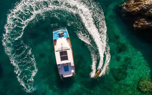 Aerial view of a catamaran and jet ski making waves in clear turquoise adriatic sea near Dubrovnik. Summer vacation scene.