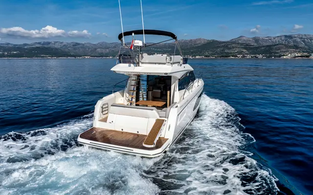 Luxury yacht cruising crystal blue Adriatic waters near Dubrovnik, Croatia, with stunning mountain backdrop under a clear sky.