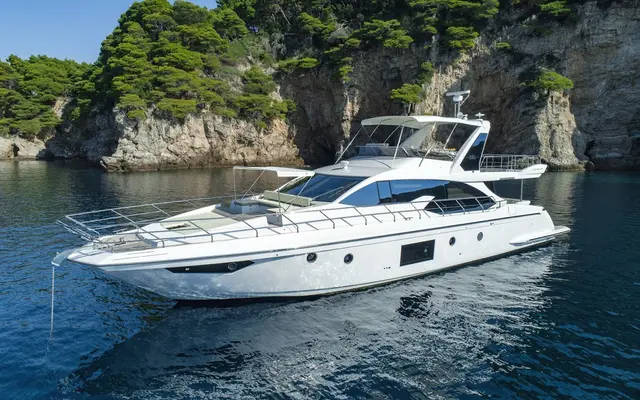 Azimut 66 Fly luxury yacht anchored in clear blue Adriatic waters near a lush green, rocky coastline in Croatia.