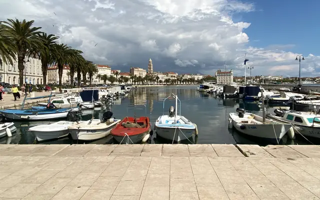 Split city harbor on the Dalmatian coast with boats, a palm-lined promenade, and historic architecture under a bright sky. Ideal departure for boat tours.