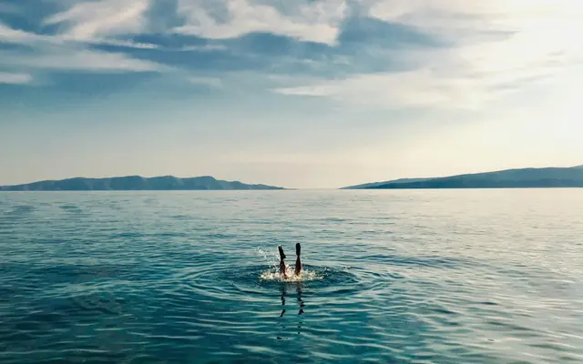 Person diving into the clear turquoise Adriatic Sea with distant islands, showcasing a refreshing private boat tour experience in Croatia.