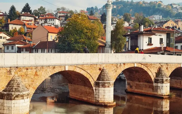 Bridge over the Miljacka River at sunrise with mosque minarets and Sarajevo old town buildings reflected in the calm water, Bosnia