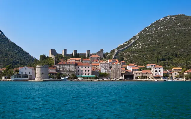 Ston town waterfront with stone buildings, round medieval defensive tower and ancient walls climbing the green hillside, Dalmatia, Croatia