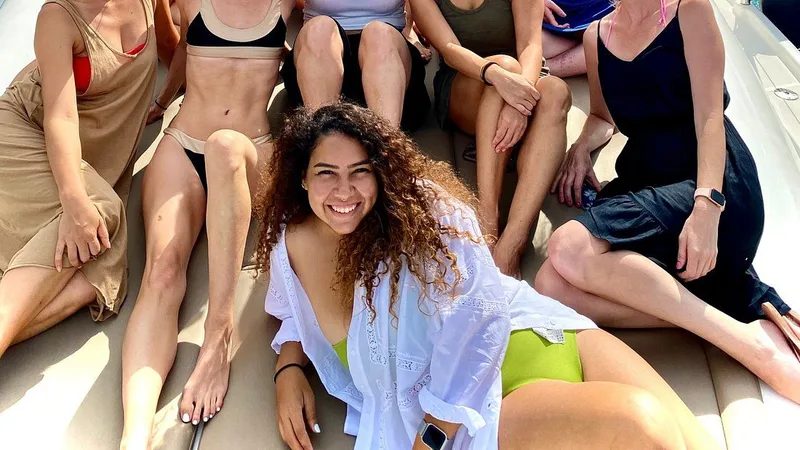 Twelve adults smile for a photo on the deck of a motor yacht, with sparkling turquoise water visible behind them.