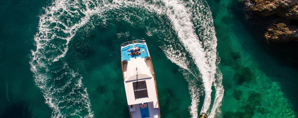Aerial view of a catamaran and jet ski making waves in clear turquoise adriatic sea near Dubrovnik. Summer vacation scene.