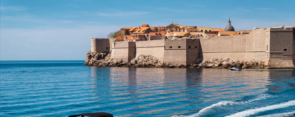 Luxury speedboat cruising on the blue Adriatic Sea with historic Dubrovnik city walls and Old Town in the background, Croatia.
