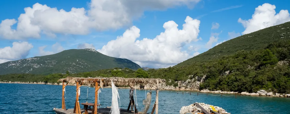 Oyster farming raft floating on calm turquoise Mali Ston Bay with a lone worker tending nets and oyster clusters, Croatia
