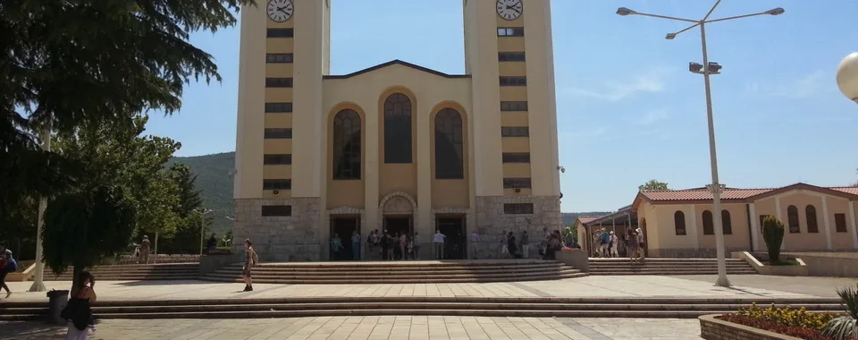 Crowd of pilgrims gathered around the Virgin Mary statue on Apparition Hill with panoramic village view