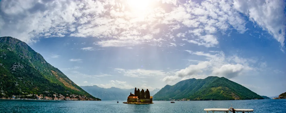 Small passenger boat on turquoise Bay of Kotor with Saint George island monastery in background near Perast