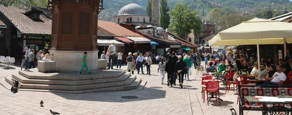 Tourists walking through Baščaršija square in Sarajevo old town with the Ottoman bazaar and Sebilj fountain area visible, Bosnia