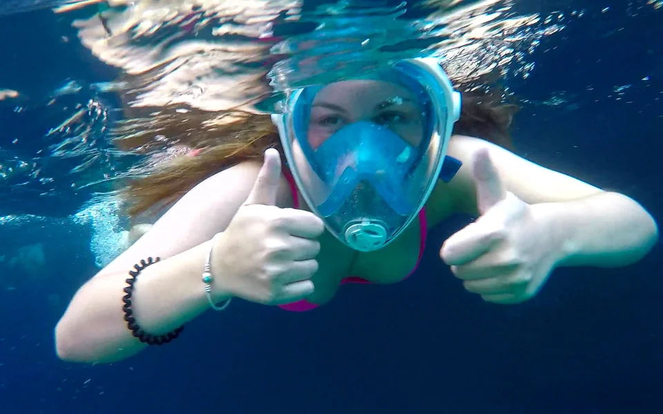Client on the private boat journey underwater wearing full-face mask gives thumbs up sign.