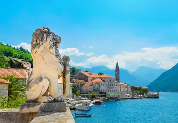 Stone lion statue on waterfront terrace with village of Perast and Bay of Kotor in background, Montenegro