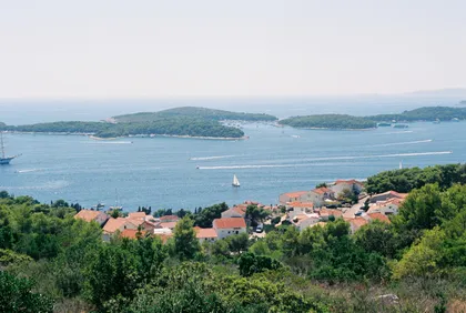 Panoramic view of Hvar, Croatia's stunning Adriatic Sea, with luxury yachts, green islands, and a charming red-roofed coastal village.