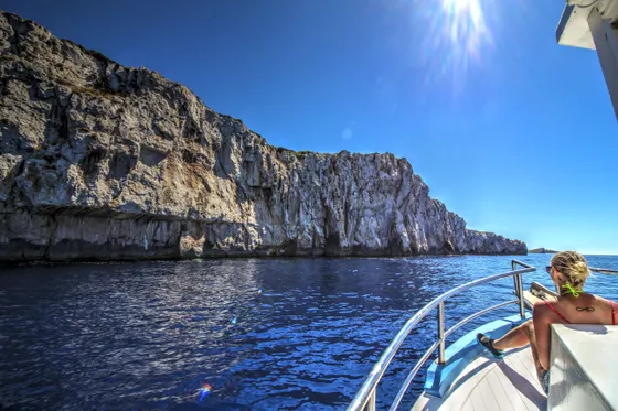 Woman relaxes on boat cruising past sunny Croatian cliffs near Dubrovnik.