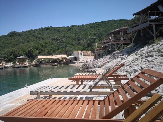Tranquil bay with wooden lounge chairs on rocky shore, overlooking crystal-clear waters and lush green hillside in Elafiti Islands