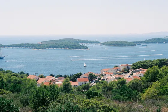 Panoramic view of Hvar, Croatia's stunning Adriatic Sea, with luxury yachts, green islands, and a charming red-roofed coastal village.