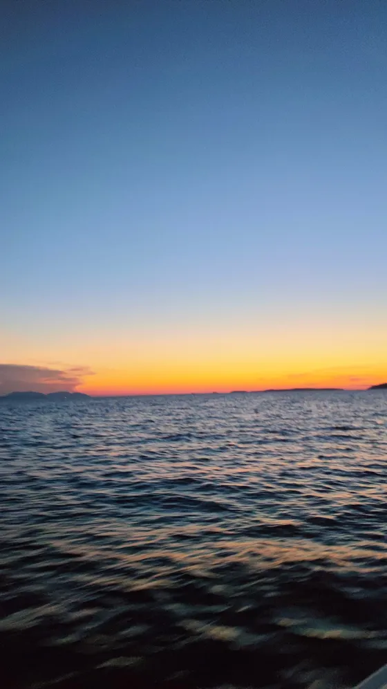 Serene sunset over calm sea with distant islands silhouetted against colorful sky gradient