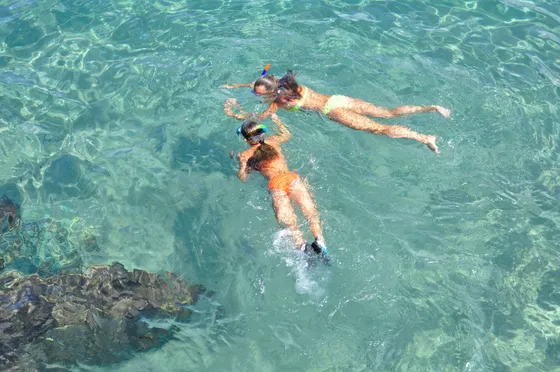 Two people snorkeling in crystal-clear turquoise waters near Blue Cave on a sunny day.