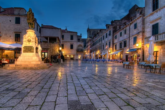 People dining and strolling on the historic Stradun main street of Dubrovnik Old Town at night with glowing lanterns, Croatia