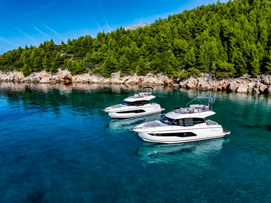 Two luxury motor yachts anchored in crystal-clear blue waters off the lush green coast of Dubrovnik, Croatia.