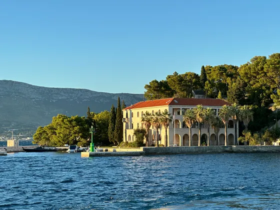 Elegant building with red roof and palm trees on the Croatian Adriatic coast, viewed from a luxury yacht. Ideal for Split charters.