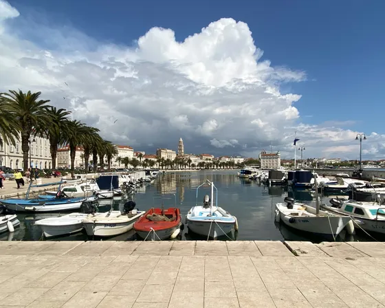 Split city harbor on the Dalmatian coast with boats, a palm-lined promenade, and historic architecture under a bright sky. Ideal departure for boat tours.