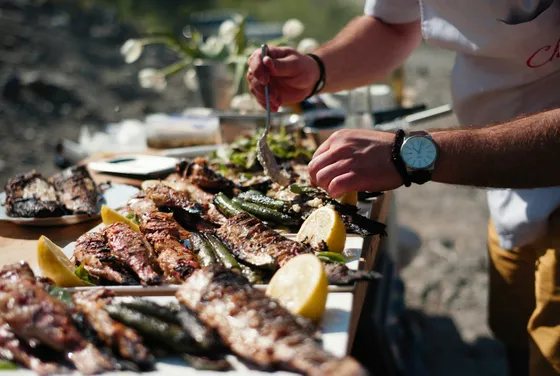Close-up of a man serving freshly grilled fish and vegetables with lemon at an outdoor Mediterranean dining experience.