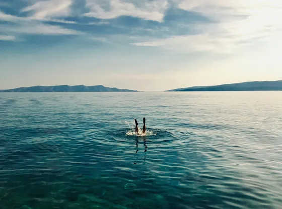 Person diving into the clear turquoise Adriatic Sea with distant islands, showcasing a refreshing private boat tour experience in Croatia.