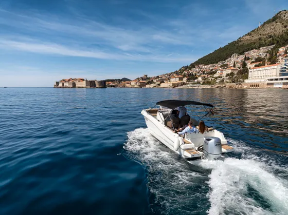 Luxury boat cruising blue Adriatic Sea with Dubrovnik Old Town city walls and scenic coastline in Croatia.