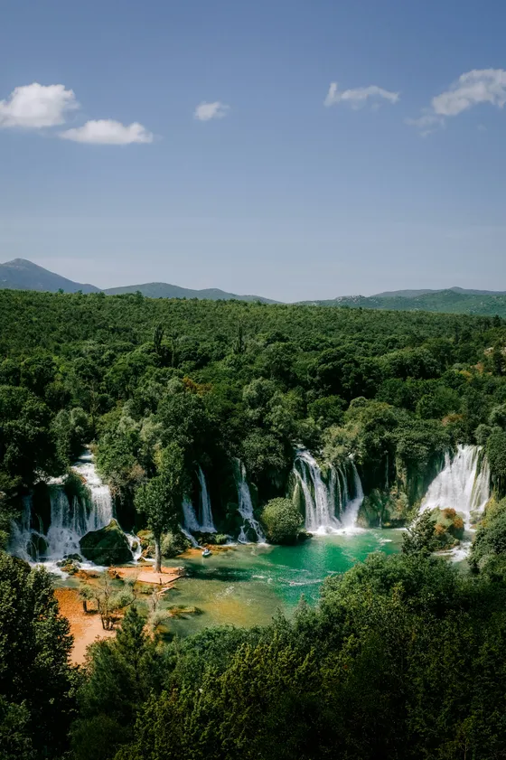 Turquoise swimming pool beneath Kravice Waterfalls on a sunny summer day in Bosnia and Herzegovina
