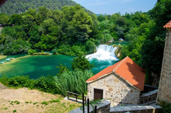 Historic stone mill with terracotta roof beside a waterfall cascading into emerald green pool at Skradinski Buk, Krka National Park, Croatia