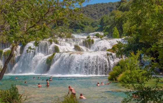 Tourists swimming in crystal-clear turquoise pool beneath Skradinski Buk waterfall at Krka National Park, Dalmatia, Croatia