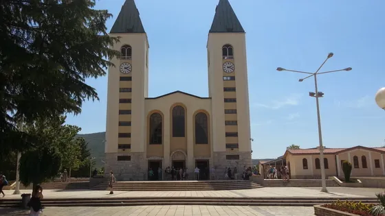 Crowd of pilgrims gathered around the Virgin Mary statue on Apparition Hill with panoramic village view