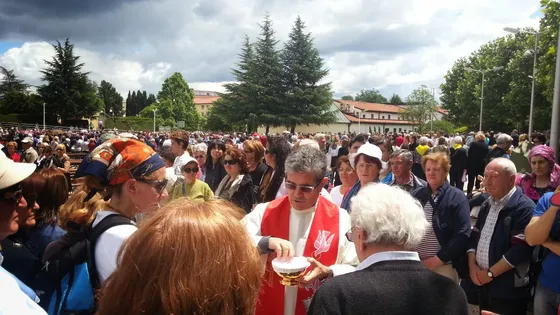 Outdoor Mass in Medjugorje with a priest distributing Holy Communion to a large crowd of pilgrims