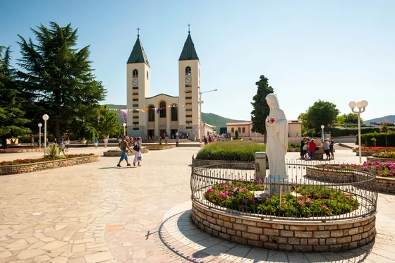 St. James Church in Medjugorje with the Virgin Mary statue in the foreground, garden and square
