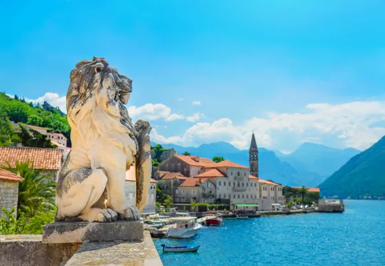Stone lion statue on waterfront terrace with village of Perast and Bay of Kotor in background, Montenegro