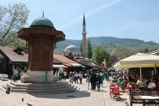 Tourists walking through Baščaršija square in Sarajevo old town with the Ottoman bazaar and Sebilj fountain area visible, Bosnia