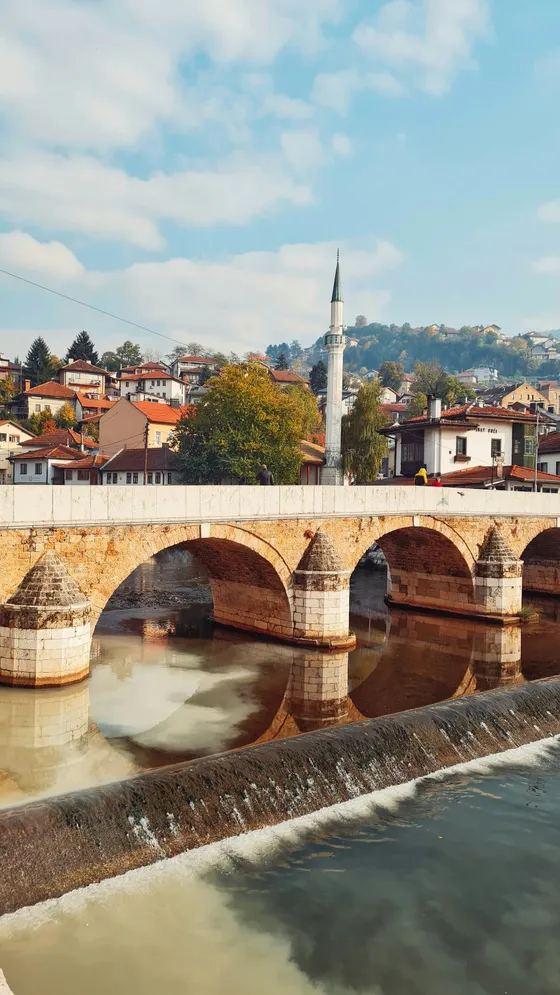 Bridge over the Miljacka River at sunrise with mosque minarets and Sarajevo old town buildings reflected in the calm water, Bosnia