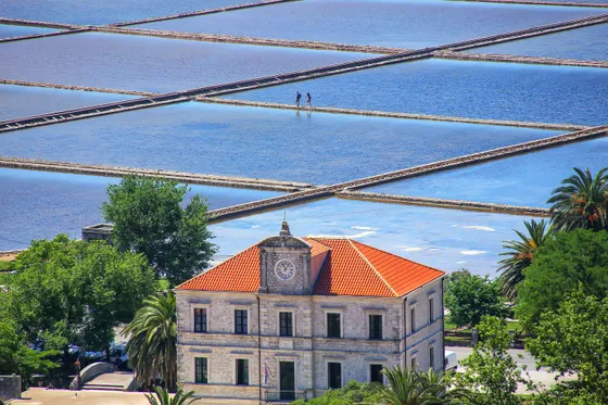 Aerial view of Ston salt pans geometric grid of evaporation pools with two workers and historic stone administrative building, Croatia