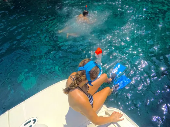 Client with snorkeling gear (included in all our boat tours) sitting on boat edge, ready to snorkel into crystal-clear turquoise waters