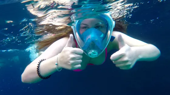 Client on the private boat journey underwater wearing full-face mask gives thumbs up sign.