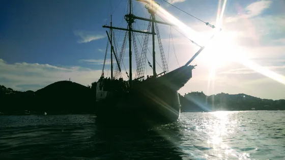Historic sailing ship silhouetted against sunset in Dubrovnik harbor, offering unique adventure cruises along Croatian coast