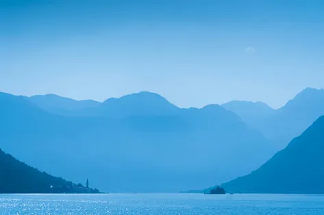 Layered misty blue mountains over the Bay of Kotor with the bell tower of Perast visible on the shoreline, Montenegro