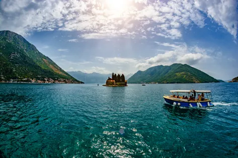 Small passenger boat on turquoise Bay of Kotor with Saint George island monastery in background near Perast