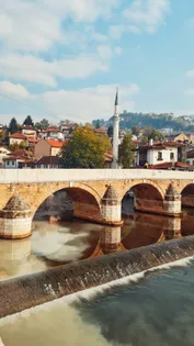 Bridge over the Miljacka River at sunrise with mosque minarets and Sarajevo old town buildings reflected in the calm water, Bosnia