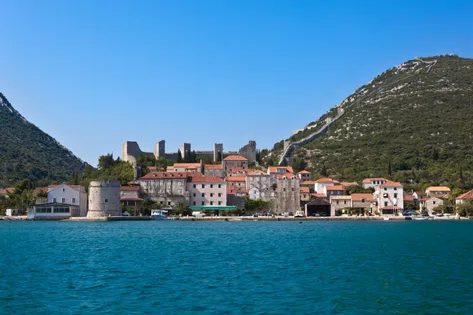 Ston town waterfront with stone buildings, round medieval defensive tower and ancient walls climbing the green hillside, Dalmatia, Croatia