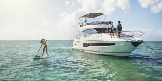 Prestige 420 luxury yacht anchored in Croatia's Adriatic Sea. A woman paddleboards while guests relax on the flybridge.