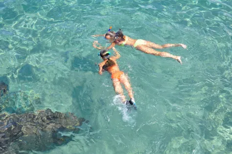 Two people snorkeling in crystal-clear turquoise waters near Blue Cave on a sunny day.
